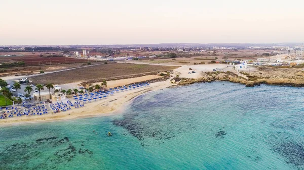 Kıyı şeridi günbatımı ve tarihi plaj manzarası yukarıdan Agia Thekla, Ayia Napa, Famagusta, Kıbrıs. Kuş bakışı gökyüzü manzarası turistlerin ilgi odağı altın kumlu körfez, adacık, Ammochostos 'taki güneşli yataklar..