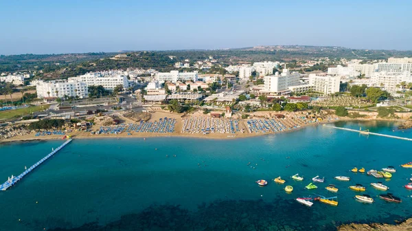 Aerial bird\'s eye view of Fig tree bay in Protaras, Paralimni, Famagusta, Cyprus. The famous tourist attraction family golden sandy beach with boats, sunbeds, restaurants, water sports, people swimming in sea on summer holidays, from above.