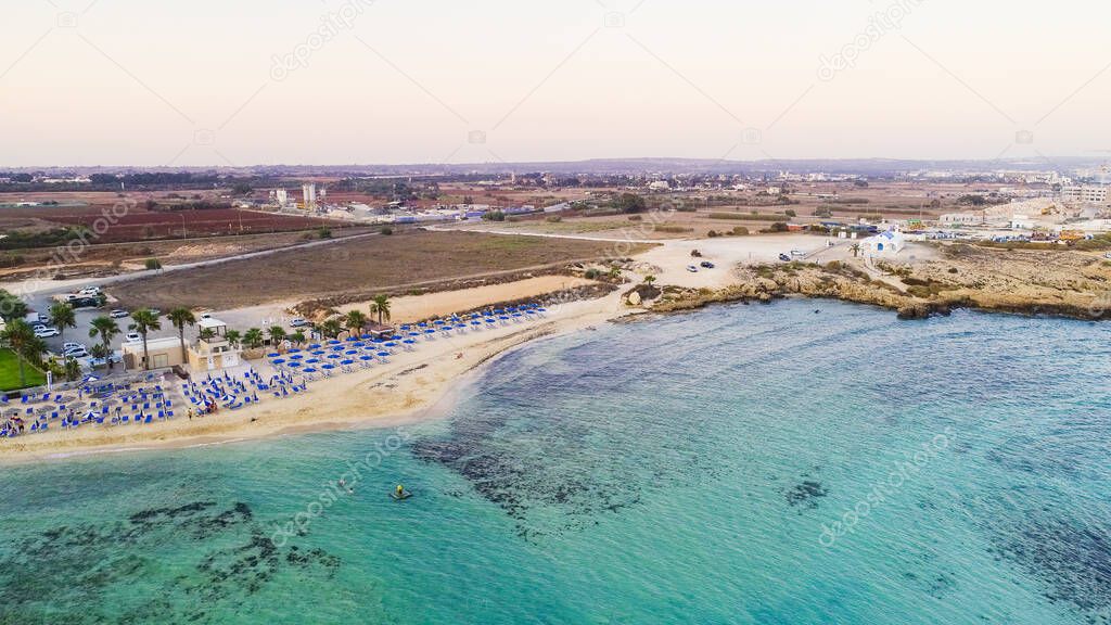 Aerial view of coastline sunset and landmark beach of Agia Thekla, Ayia Napa, Famagusta, Cyprus from above. Bird's eye skyline view of tourist attraction golden sand bay, islet, sunbeds in Ammochostos.