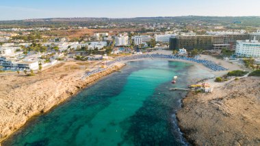 Vathia Gonia plajı, Ayia Napa, Famagusta, Kıbrıs 'ın havadan kuş bakışı görüntüsü. Gündoğumunda, Agia Napa 'da yaz tatillerinde altın kum, güneşlik, deniz restoranları ve deniz restoranlarıyla turistik bölge kayalık körfezi..