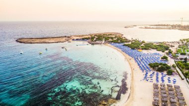 Ünlü Makronissos sahil şeridi Ayia Napa, Famagusta, Kıbrıs 'ın havadan kuş bakışı manzarası. Günbatımında Agia Napa 'da altın kum, güneşlik, deniz restoranları ve yaz tatilleri ile turistik mekan Makronisos Körfezi..