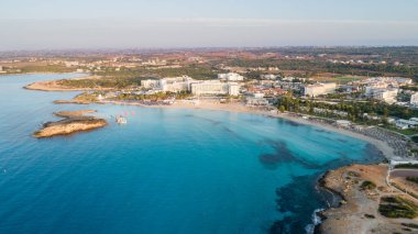 Ünlü Nissi sahil şeridi Ayia Napa, Famagusta, Kıbrıs 'ın havadan kuş bakışı manzarası. Gündoğumunda, Agia Napa 'da yaz tatillerinde altın kum, güneşlik yataklar ve deniz restoranlarıyla birlikte turistik bölge körfezi..