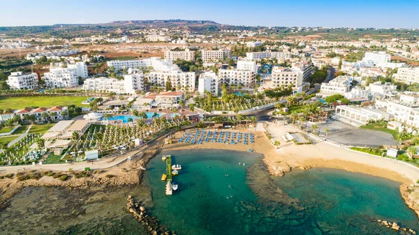 Aerial bird\'s eye view of Pernera beach in Protaras, Paralimni, Famagusta, Cyprus. The famous tourist attraction golden sandy bay with sunbeds, water sports, hotels, restaurants, people swimming in sea on summer holidays from above.