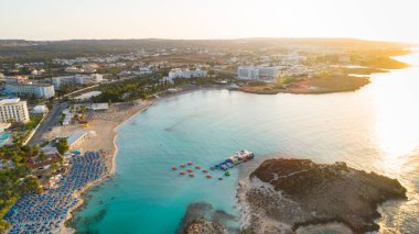 Ünlü Nissi sahil şeridi Ayia Napa, Famagusta, Kıbrıs 'ın havadan kuş bakışı manzarası. Gündoğumunda, Agia Napa 'da yaz tatillerinde altın kum, güneşlik yataklar ve deniz restoranlarıyla birlikte turistik bölge körfezi..
