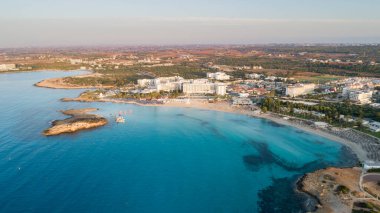 Ünlü Nissi sahil şeridi Ayia Napa, Famagusta, Kıbrıs 'ın havadan kuş bakışı manzarası. Gündoğumunda, Agia Napa 'da yaz tatillerinde altın kum, güneşlik yataklar ve deniz restoranlarıyla birlikte turistik bölge körfezi..