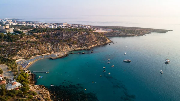 Aerial bird\'s eye view of Konnos beach in Cavo Greco Protaras, Paralimni, Famagusta, Cyprus. The famous tourist attraction golden sandy Konos bay with boats, yachts, sunbeds, water sports, people swimming in sea on summer holidays, from above.