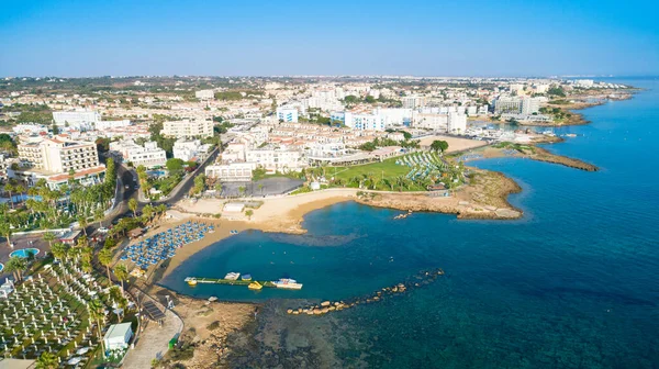 Aerial bird\'s eye view of Pernera beach in Protaras, Paralimni, Famagusta, Cyprus. The famous tourist attraction golden sandy bay with sunbeds, water sports, hotels, restaurants, people swimming in sea on summer holidays from above.