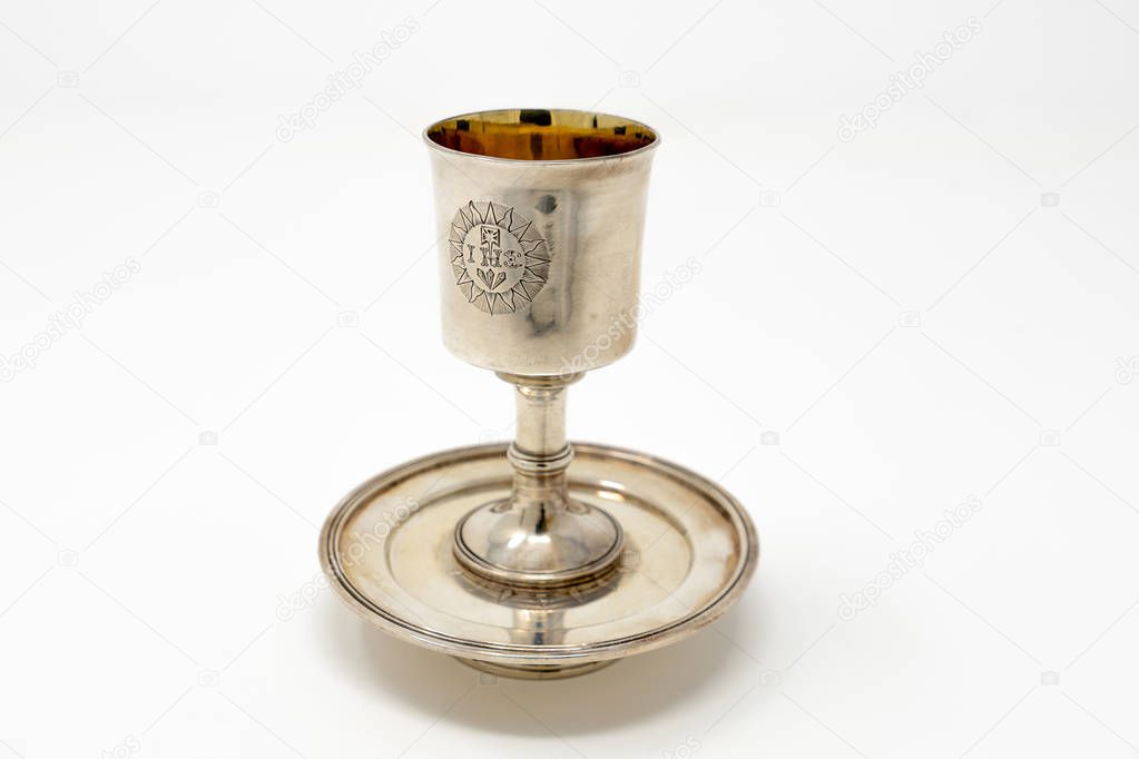 A stirling silver communion chalice to hold the wine during Holy Communion services, with a golden lining and set on top of a silver paten against a white background
