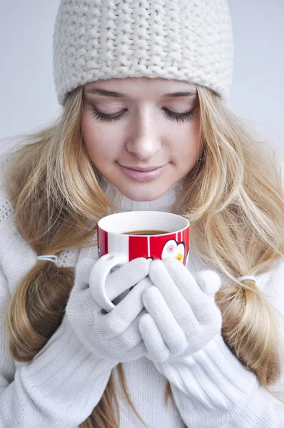 Beautiful blond young woman in winter gloves and hat holding cup of coffee