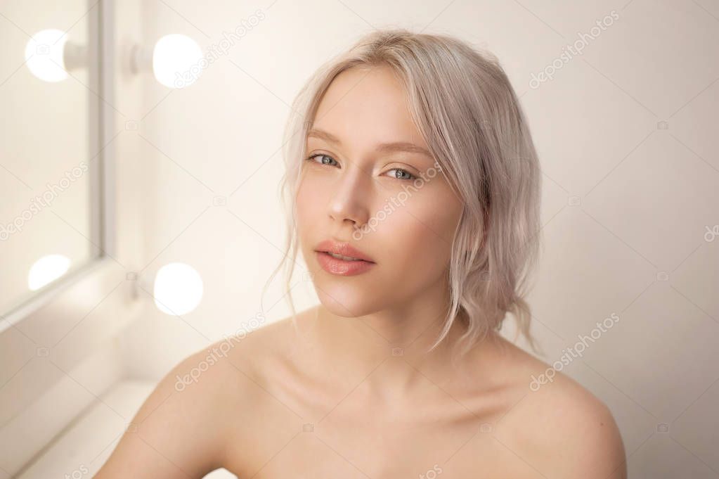 Beautiful young woman with clean fresh skin sitting in white studio with mirror