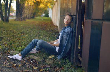 tam uzunlukta şık sarışın genç çocuk Binası yakınındaki çimenlerin üzerinde oturan açık portresi