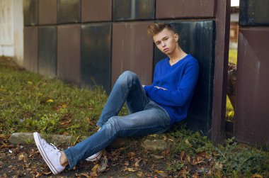 tam uzunlukta şık sarışın genç çocuk Binası yakınındaki çimenlerin üzerinde oturan açık portresi