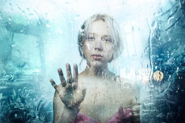 Genç güzel sarışın kız yağmur ile cam arkasında, gerçeküstü portresi el ile dokunmak bırakır. Kavram