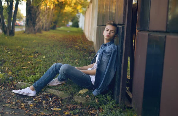 tam uzunlukta şık sarışın genç çocuk Binası yakınındaki çimenlerin üzerinde oturan açık portresi