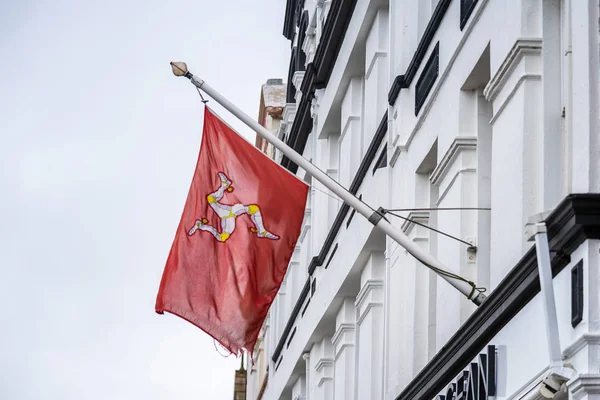 La bandera de la Isla de Man o bandera de Mann es un triskelion, compuesto por tres patas blindadas con espuelas doradas, sobre un fondo rojo. — Foto de Stock