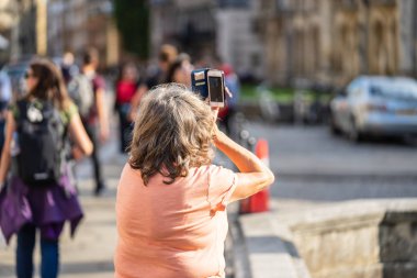 Cambridge, İngiltere, 1 Ağustos 2019. Kings Koleji önünde güneşli bir günde Cambridge caddesinde yürüyen ve fotoğraf çeken turistler