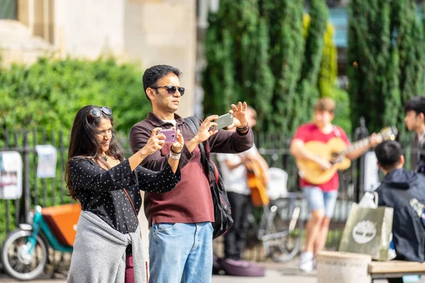 Cambridge, İngiltere, 1 Ağustos 2019. Kings Koleji önünde güneşli bir günde Cambridge caddesinde yürüyen ve fotoğraf çeken turistler