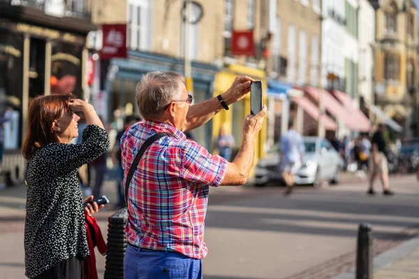 Cambridge, İngiltere, 1 Ağustos 2019. Kings Koleji önünde güneşli bir günde Cambridge caddesinde yürüyen ve fotoğraf çeken turistler
