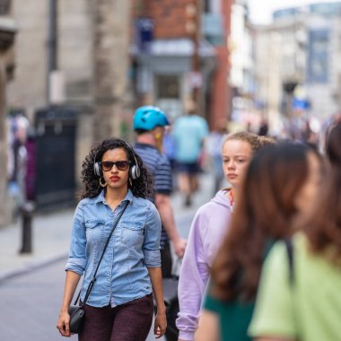 Cambridge, İngiltere, 1 Ağustos 2019. Şehirde akıllı telefon mobil teknolojisini kullanarak kulaklık takan müzik dinleme keyfini güzel karışık ırk kadın Portresi