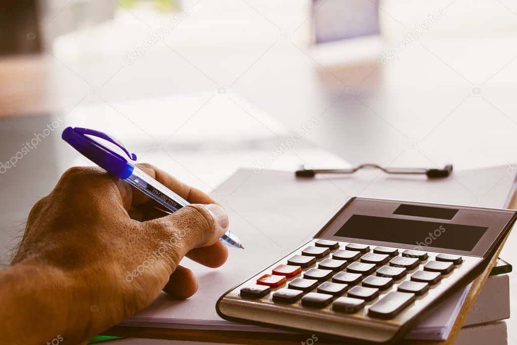 Asian man writing or pressing calculator for business finance on blurry background.for accounting, business, finance 