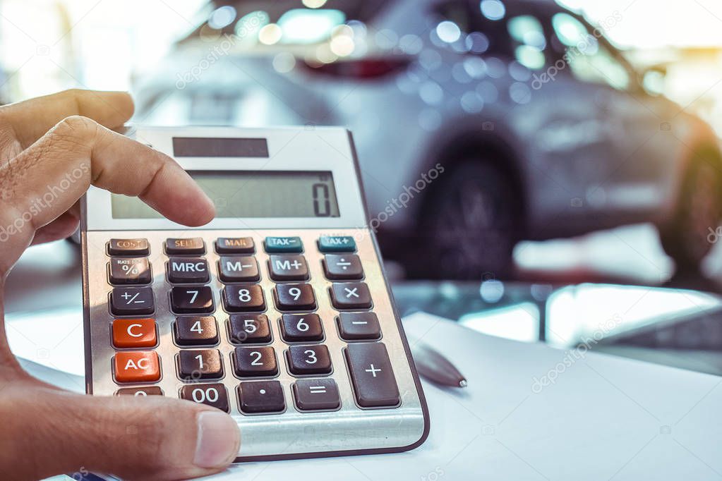 Asian man pressing calculator for business finance on car showroom blurry background.for automotive or transportation