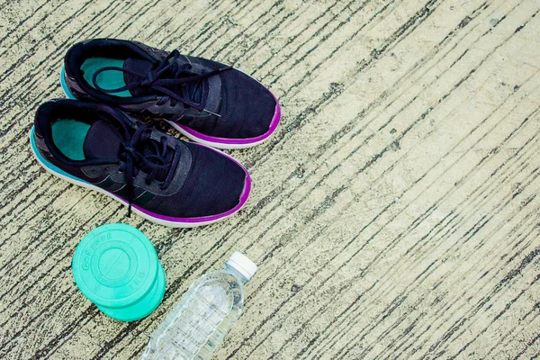 Sports shoes with bottle and green color dumbbell on the floor or street Metaphor Fitness and workout concept exercise Health lifestyle muscle with  take care of your health copy for advertising