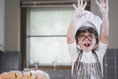 Asyalı çocuk beyaz unla yemek pişirirken gözlük takıyor. Ekmek hamuru eğiyor. Çocuklara ekmek pişirmeyi öğretiyor.