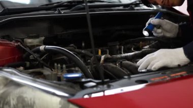 Beyaz eldivenli bir oto tamircisi bir arabanın içini ve motorunu kontrol ediyor.