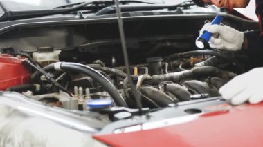 Beyaz eldivenli bir oto tamircisi bir arabanın içini ve motorunu kontrol ediyor.