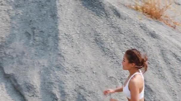 白いトップと黒いショートパンツのスポーティーな女の子が岩を駆け上がっています アクティブライフスタイルコンセプト — ストック動画