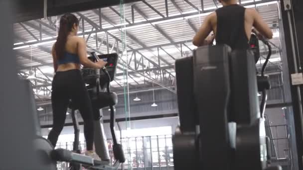 男性と女性は 楕円形のマシン上のジムで持久力のカーディオ演習を行う — ストック動画