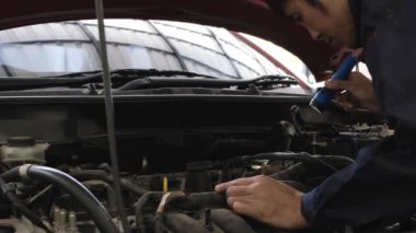Asyalı bir adamın el feneriyle arabanın motorunu kontrol ederken görüntüsü. Araba tamir istasyonu ya da teknisyen uzmanı konsepti
