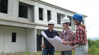 İnşaat alanını kontrol ederken yavaş görüntüler, miğferli Asyalı mühendisler inşaat sahasında dolanıp planları kontrol ediyorlar.