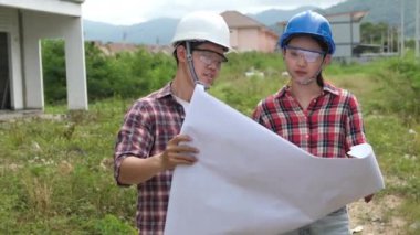 İnşaat alanını kontrol ederken yavaş görüntüler, miğferli Asyalı mühendisler inşaat sahasında dolanıp planları kontrol ediyorlar.
