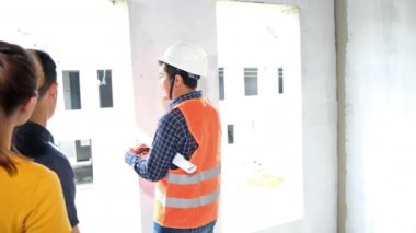 İnşaat alanını kontrol ederken yavaş görüntüler, miğferli Asyalı mühendisler inşaat sahasında dolanıp planları kontrol ediyorlar.