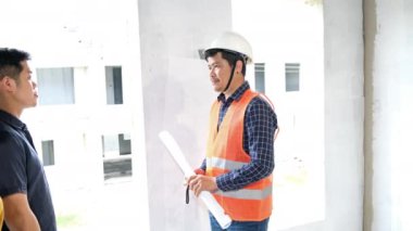 İnşaat alanını kontrol ederken yavaş görüntüler, miğferli Asyalı mühendisler inşaat sahasında dolanıp planları kontrol ediyorlar.