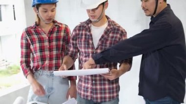 İnşaat alanını kontrol ederken yavaş görüntüler, miğferli Asyalı mühendisler inşaat sahasında dolanıp planları kontrol ediyorlar.