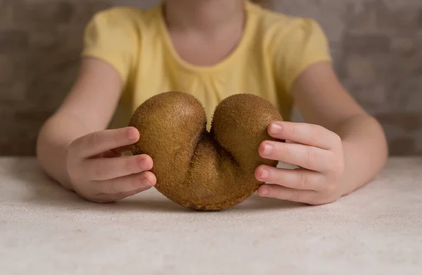 Ugly kiwi in the heart shape on a gray background. Funny, unnormal fruit or food waste concept. Horizontal orientation. Copy space.