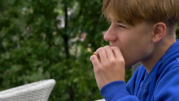 Zblízka záběr chlapce, jak jí venku. Teenager sedí v sendvičovém baru. — Stock video