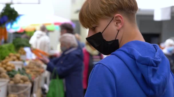 Young boy with face mask walks through food market and tries to find something fresh during quarantine. — Stock Video