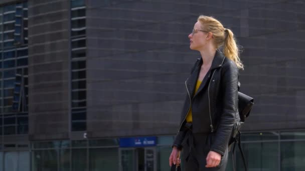 Mujer joven relajada caminando por la calle y mirando a su alrededor. Mujer con gafas va tranquilamente a trabajar . — Vídeos de Stock