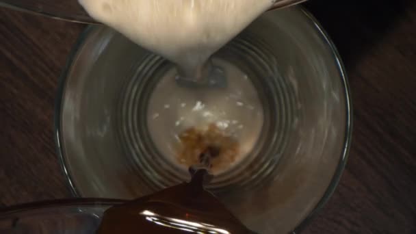 从上往下看咖啡和牛奶倒入杯子.慢镜头混合牛奶和咖啡。形成的小气泡宏观视图. — 图库视频影像
