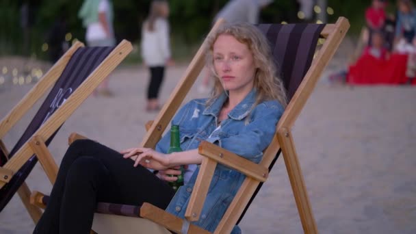 Jeune femme endormie s'assoit sur la chaise de plage et regarde l'environnement. Belle femelle tient son verre et attend le coucher du soleil. — Video