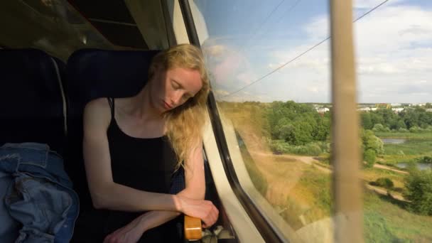 Junge Frau im Model-Look schläft im Zug. Blonde Haare Frauen reisen mit dem Zug. Schläfriger, sonniger Morgen. Blick aus dem Fenster ändern. — Stockvideo