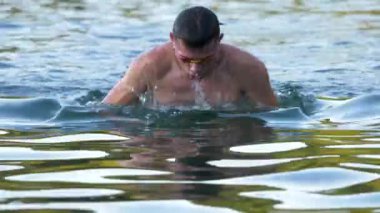 Gölde yüzen genç atleti yakından çek. Profesyonel yüzücü trenleri dışarıda. Güneşli bir gün, berrak su. Çekim.