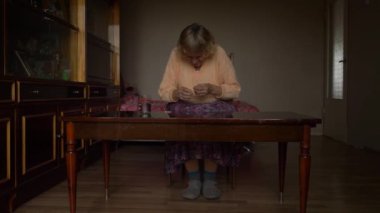 Yaşlı kadının eski Sovyet odasında oturup ilaç tabletlerini günlük kullanım için kontrol etmeye çalışmasını yavaş çekim yap..