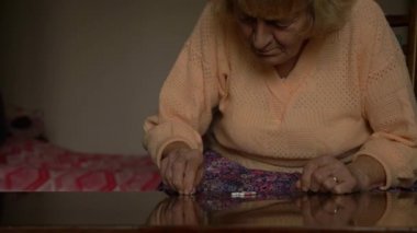 Yaşlı kadın ilaç tabletlerine bakar ve doğru ilacı bulmaya çalışır. Sarı saçlı, kırışık ve alyanslı büyükanne..