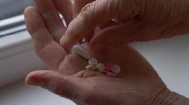 Kırış kırış olmuş eski elin avuç içinden ilaç tabletlerini alırken yakın çekim. Kıdemli kadın elleri..