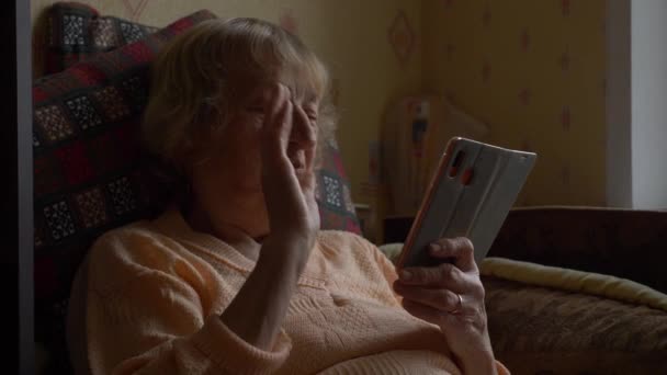 La abuela saluda a sus nietos durante la comunicación a distancia. Una mujer mayor durante la cuarentena no puede ir a visitar a su familia. Vista oscura. — Vídeos de Stock