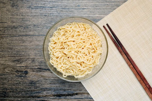 木製テーブルの上の箸に近いガラスのボウルでインスタント麺のトップ ビュー — ストック写真